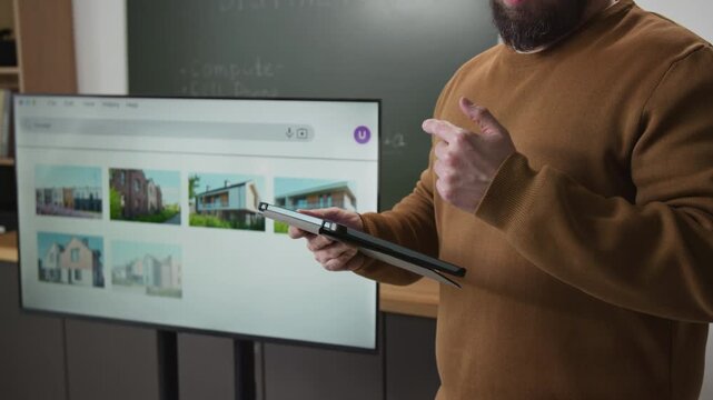 Side view close up shot of unrecognizable male teacher holding tablet in hands and talking in computer literacy class with screen showing web browser in background, copy space