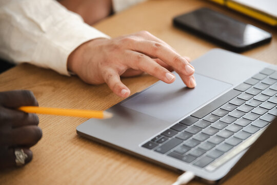 Two people collaborate at a desk, one using a laptop and the other holding a pencil, suggesting teamwork and productivity.