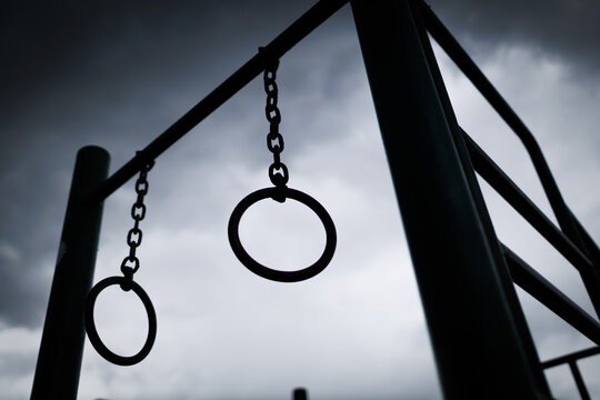 metal exercise rings hang from a frame against a dark sky filled with clouds before a storm in a park