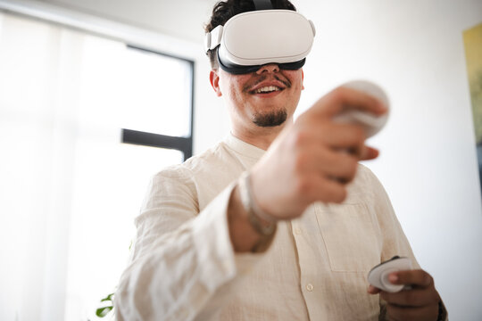 A man wearing a virtual reality headset smiles as he holds controllers, engaging with an immersive digital experience.