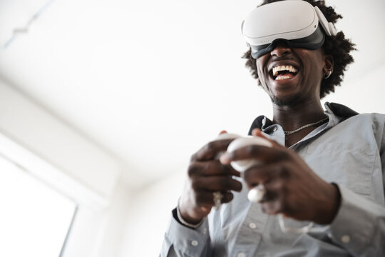 A man wearing a virtual reality headset laughs while holding controllers, immersed in a digital experience.