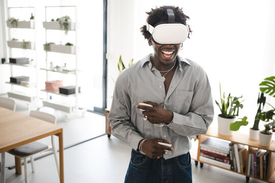 A young man wearing a virtual reality headset and holding controllers laughs while experiencing immersive technology in a modern, bright room.