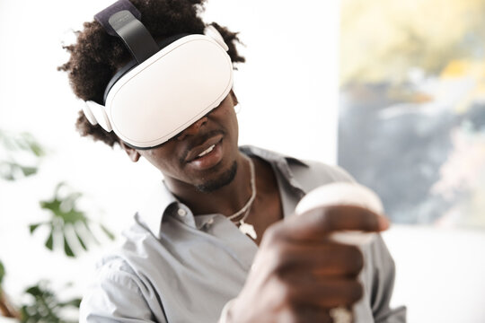 A young man wearing a virtual reality headset and holding a controller interacts with a digital world, experiencing immersive technology.
