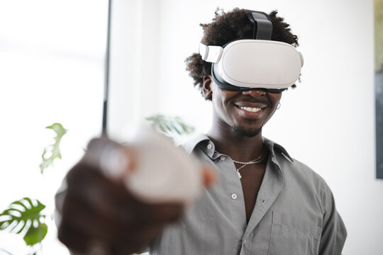 A smiling man wearing a virtual reality headset and holding a controller, immersed in a digital world.