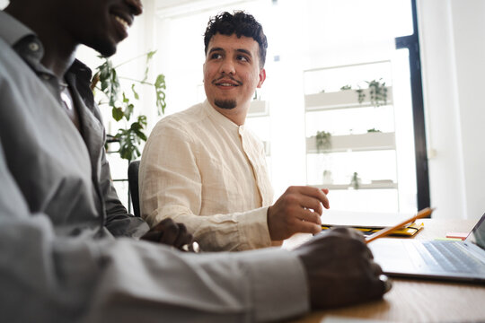 Two men collaborate on a project at a desk with a laptop and papers, discussing ideas and working together.