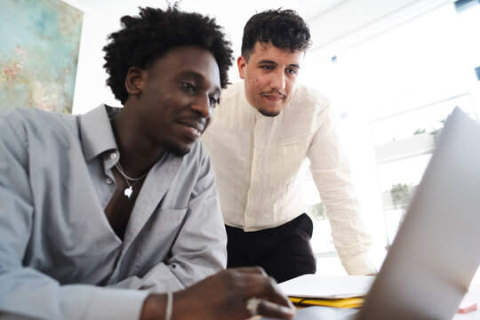 Two men collaborate on a project, one looking at a laptop screen while the other leans in to observe.