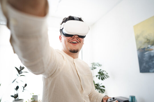 A man wearing a virtual reality headset and holding a controller smiles as he experiences an immersive digital world.