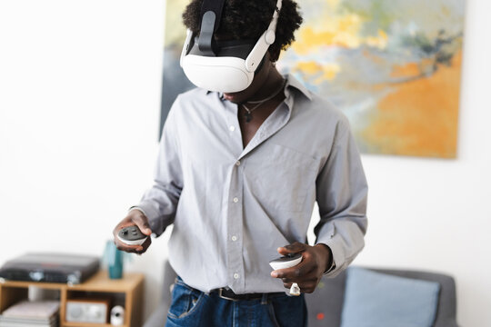 A young man wearing a virtual reality headset and holding controllers engages with immersive technology in a living room setting.