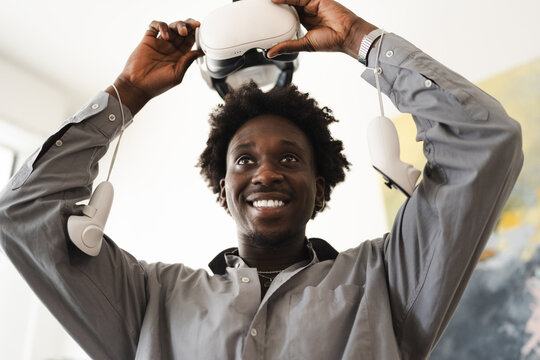 A man smiles as he holds a virtual reality headset above his head, with controllers in each hand.