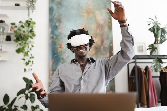 A man wearing a virtual reality headset smiles as he gestures with his hands, immersed in a digital experience.