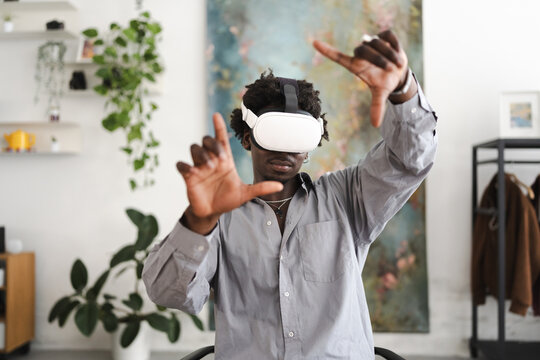 A young man wearing a virtual reality headset interacts with a digital world, his hands gesturing as he explores an immersive experience.