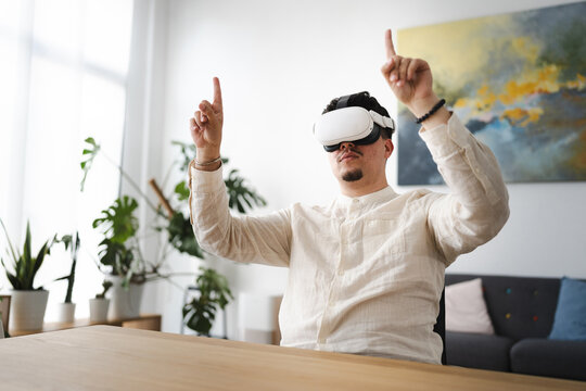 A man wearing a virtual reality headset raises his hands and points his fingers upwards, engaging with an immersive digital experience.