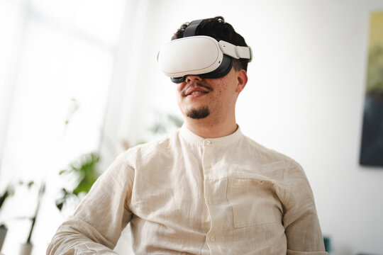 A man wearing a virtual reality headset experiences immersive technology. He is dressed in a light-colored collared shirt, looking to the side with a slight smile.
