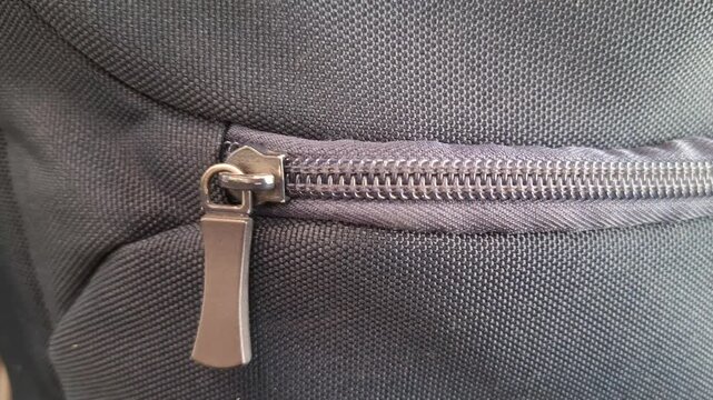 Close-up of dark grey metallic zipper on nylon bag. Fabric with sturdy zip fastener. Accessory detail for fashion, luggage, and outerwear industries. Closed zipper puller on rugged synthetic material