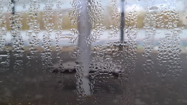 Condensation on train window pane overlooking blurred railway station platform. Atmosphere of travel and departure. Water droplets texture with foggy background of perron. Artistic urban view