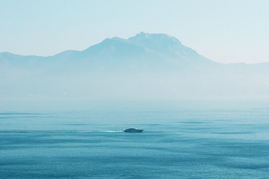 Boat Travels Across Water While Mountains Rise in the Background During Bright Daylight Hours
