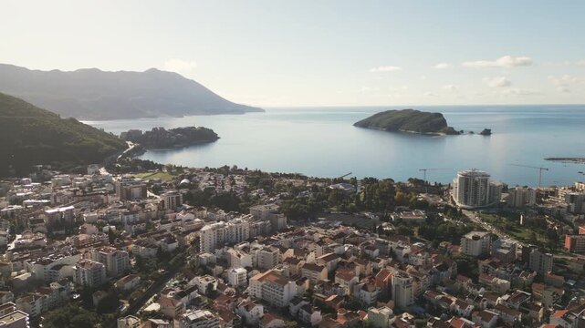 Cinematic aerial pull-back and rotation revealing Budva city panorama and Adriatic sea in Montenegro. Warm morning sun illuminating the cityscape and coastline.