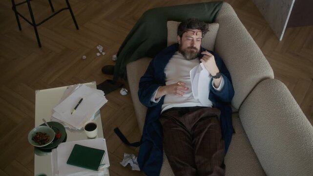 From above view of middle aged Caucasian writer wearing robe and eyeglasses sleeping in messy living room, then waking up and immediately taking notes