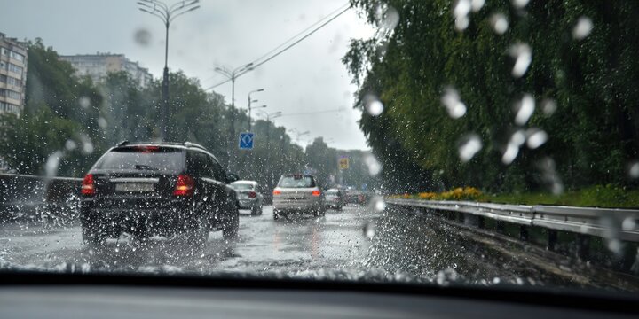 View through wet windshield of city road with cars during heavy rain