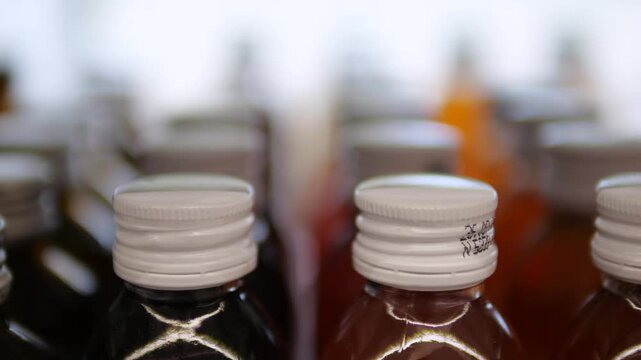 Close up view of numerous glass bottles filled with various juices and sealed with white screw caps, neatly arranged in rows on a shelf with a soft, out of focus background