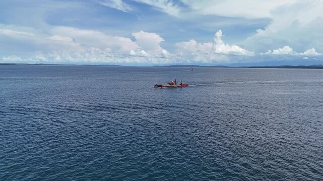 A working construction barge moves steadily across the deep blue waters of Bocas del Toro, Panama, carrying piles of sand and heavy machinery. 