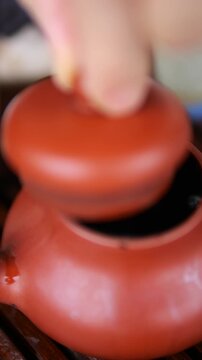 Close up of a hand placing the lid on a traditional red clay teapot filled with hot, bubbling pu erh tea, part of an ancient chinese gongfu tea ceremony for health and relaxation