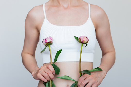 Young caucasian woman holding small unopened peony buds against her chest, symbolizing small breasts, embracing natural beauty and self-love.