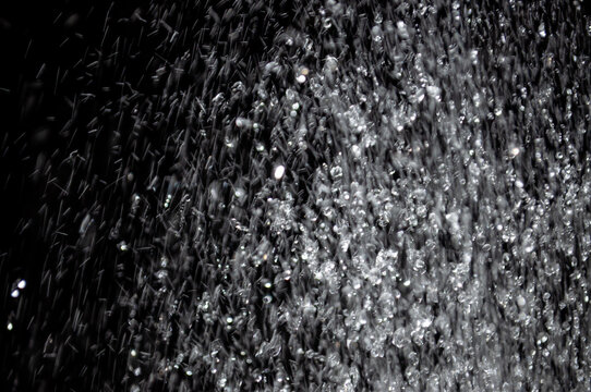 Water droplets fall from a height creating a curtain of water in a dark space at night