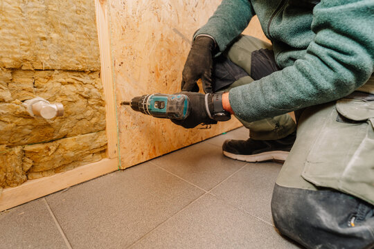Male construction worker using a power drill to install wooden panels on a wall in a residential interior setting