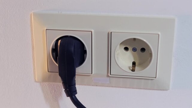 Hand inserting electrical plug into European wall outlet, connecting power supply, household electricity usage, close-up of socket installation, safe energy connection indoors