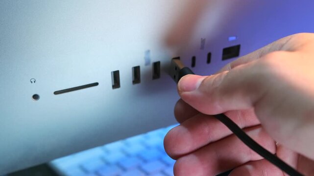 hand inserting usb cable close-up view, plugging connector into computer port on all-in-one device, data transfer and charging process, modern technology usage, workstation setup