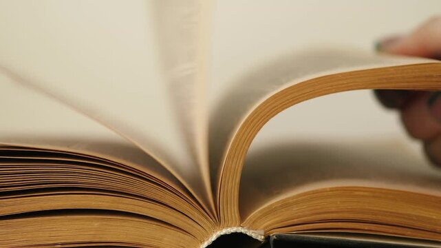 Close-up of hands quickly flipping through yellowed pages of an old vintage book. Macro shot of person searching for information in a weathered antique book.