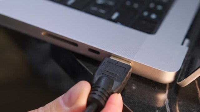 Close-up of connecting an HDMI cable to a laptop, highlighting external monitor setup, high-definition video transmission, everyday digital workflow with modern computer interfaces and display devices