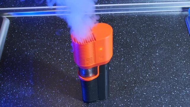 portable smoke machine emitting vapor close-up view, device releasing dense white plume through diffuser nozzle, atmospheric effect for filming and stage setup, special effects equipment in action