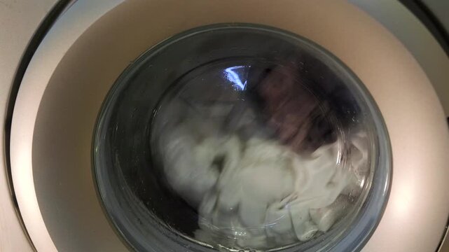 washing machine spinning clothes front view, rotating drum agitates fabric inside appliance, household cleaning process in progress, daily laundry routine, home equipment usage