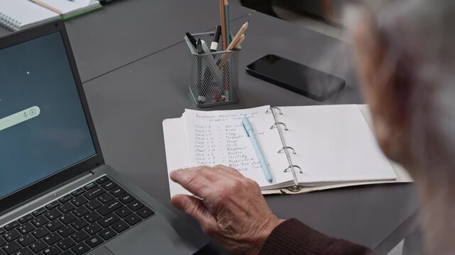 Over shoulder close up shot of unrecognizable senior woman checking notes with key shortcut combinations while sitting at desk in computer literacy class, copy space