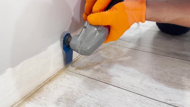 Flooring repair, laminate flooring warped due to lack of clearance, technological compensation gap, technician sawing laminate flooring with a renovator tool, video with sound.