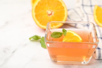 Fototapeta premium Yummy jelly in glass bowl, oranges and mint on white marble table, closeup. Space for text