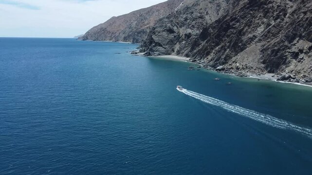 Aerial pull-away shot of a boat sailing in calm waters next to a massive mountain, La Ventana Bay, Baja California.