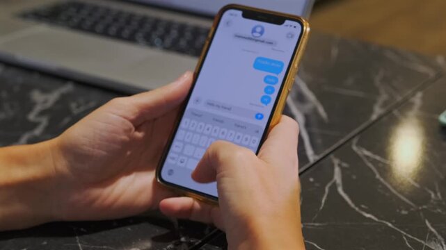 hands typing on phone keyboard close-up view, fingers tapping virtual keys while holding mobile device, digital messaging process, online communication and text input with laptop on background