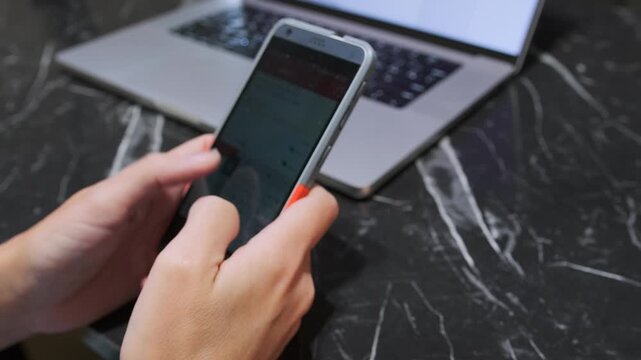 hands typing message on phone close-up view, fingers tapping screen keyboard while holding device, digital communication process, mobile texting and online interaction with laptop in background