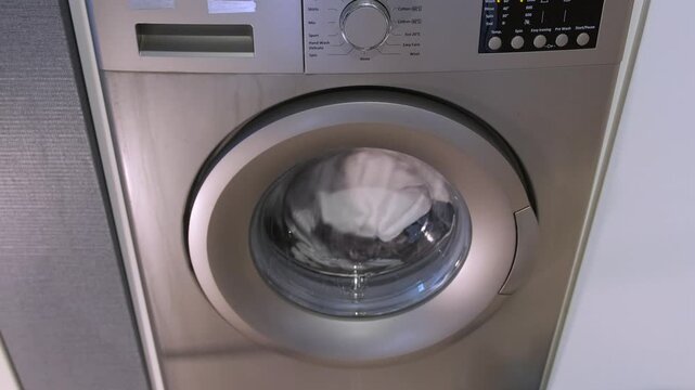 washing machine rotating clothes front view, active cleaning cycle with water and foam inside drum, continuous motion of fabric during wash program, household appliance operation and daily laundry
