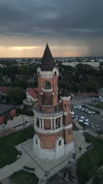 Vertical drone video orbiting the historic Gardos Tower in Zemun, Belgrade. Powerful lightning storm in the background at twilight with dark storm clouds and electric flashes illuminating the sky.