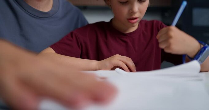 Young Male Student Tightly Holding His Pen During Focused Writing Session With Blurred Family In Backdrop