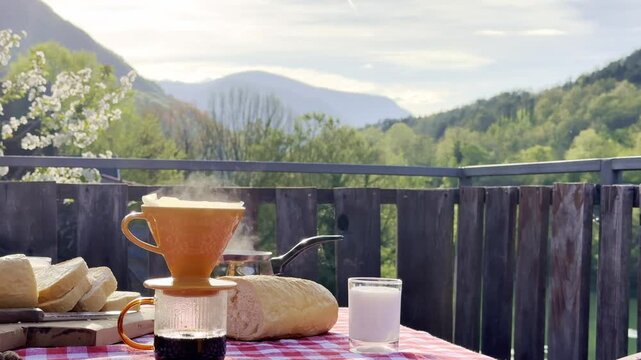 Steaming coffee prepared with pour over method served with fresh bread and milk on rustic outdoor terrace with scenic mountain view. Cozy morning breakfast in countryside with natural light and slow l