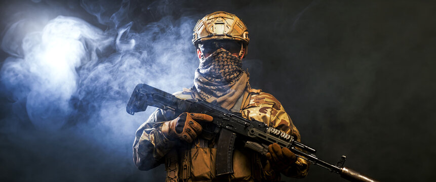 Military soldier with assault rifle standing on dark smoky background. Concept protection, conflict and security forces.
