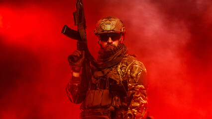Naklejka premium Military soldier with assault rifle standing on red smoky background. Concept defense, tension and security forces. 