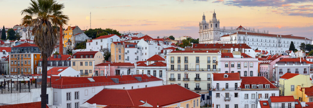 Lisbon, Portugal. Panorama of the city during sunset evening. Houses red roofs of historic old town in district Alfama in Lisboa. Palm tree in front.