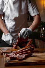 Chef cutting juicy grilled pork ribs on wooden board, close up of hands with knife slicing roasted...