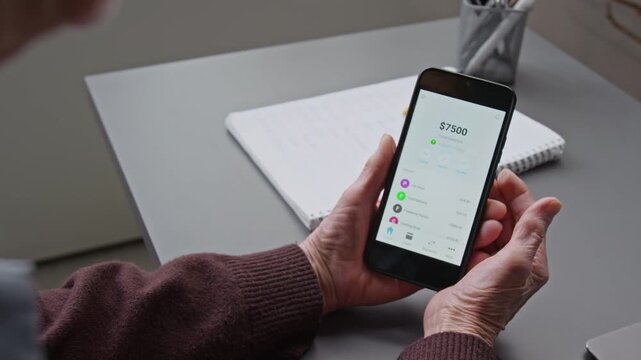 Over shoulder close up shot of unrecognizable senior woman holding phone with online banking app on screen and successfully logging in system, copy space
